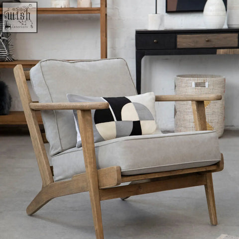 Light gray upholstered armchair with natural wood frame featuring bosie ozella circular print embroidered cushion