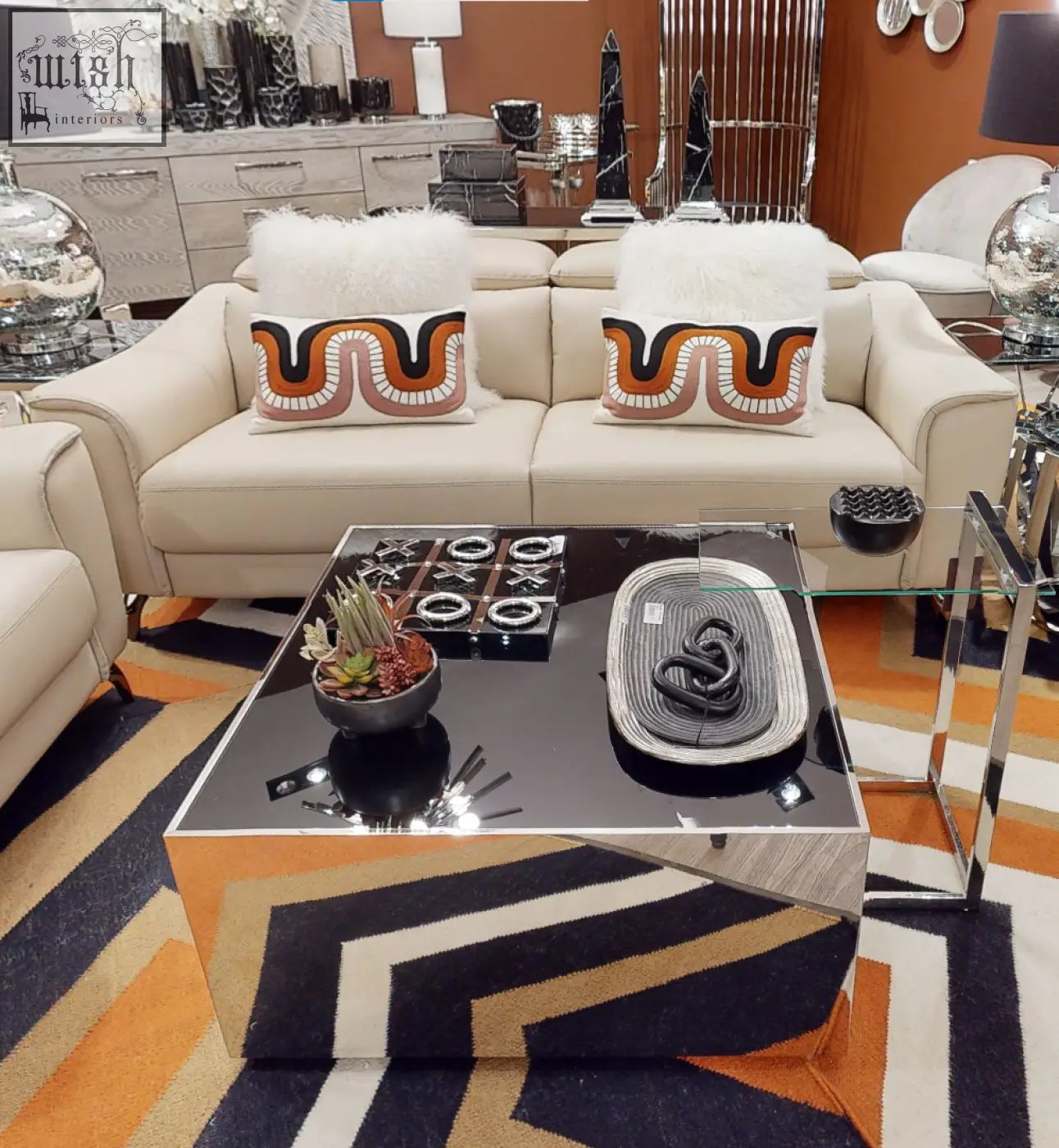 Modern black and silver mirrored coffee table with geometric chrome legs next to ozella curve pattern rectangular cushion