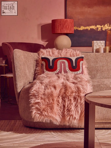 A cozy plush pink throw draped over a modern armchair featuring the ozella curve pattern rectangular cushion