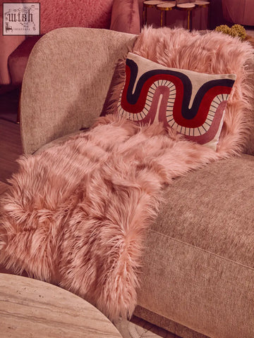 A bosie ozella curve pattern rectangular cushion with bold red and navy embroidery on a beige armchair with pink faux fur throw