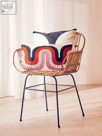 Woven rattan chair with black metal legs and colorful ozella curve pattern rectangular cushion on its seat
