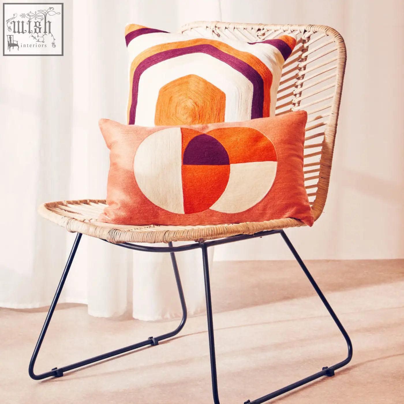 Two bosie ozella multicolour rectangular cushions in warm orange cream and deep purple on a woven rattan chair
