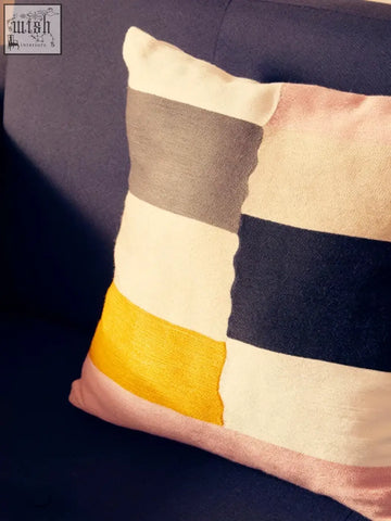 A cozy bosie ozella patch design cushion with bold cream gray navy blue yellow and soft pink stripes