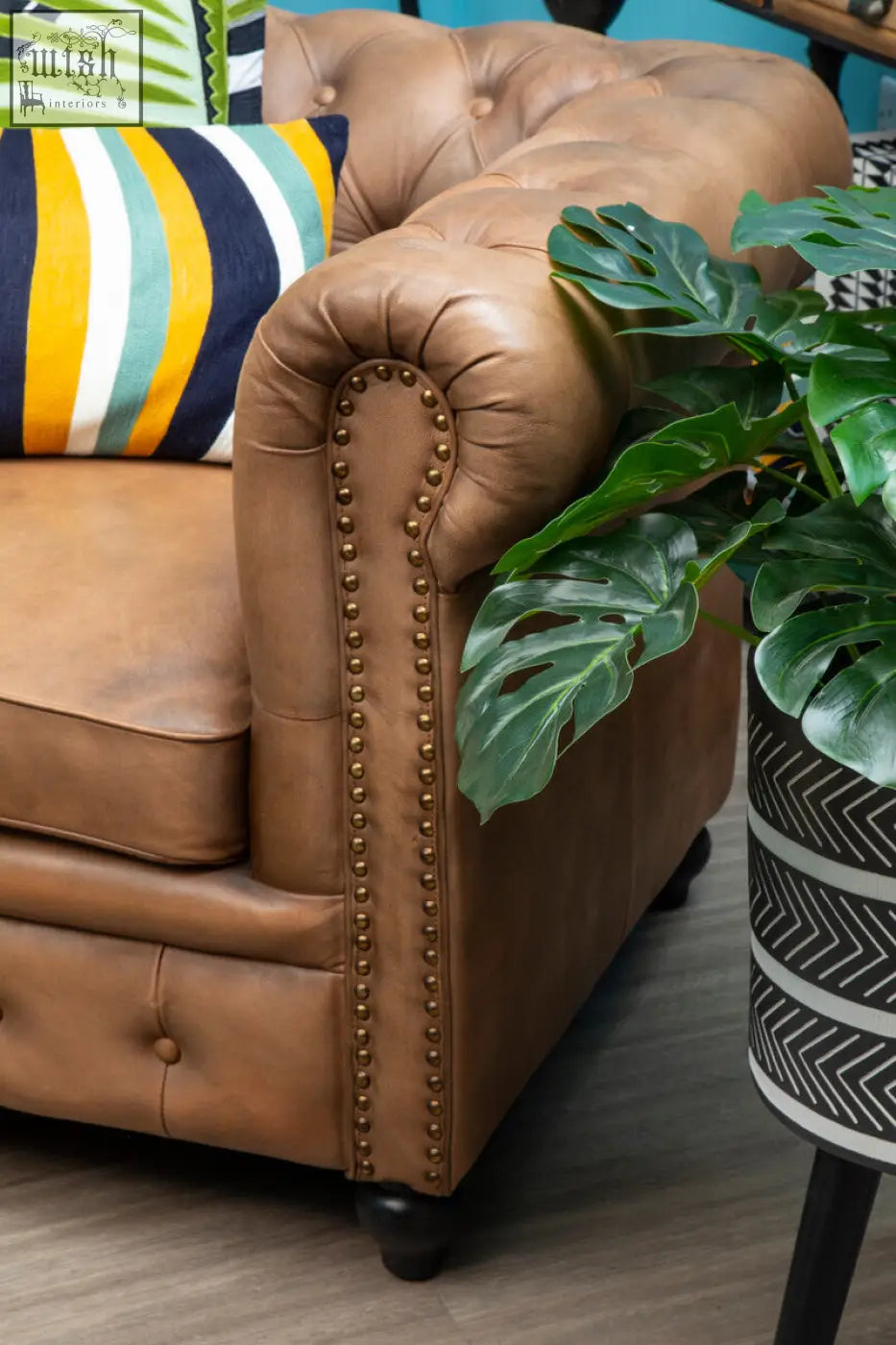 Tan leather chesterfield sofa with button tufting and brass nailhead trim featuring bosie ozella stripes design cushion