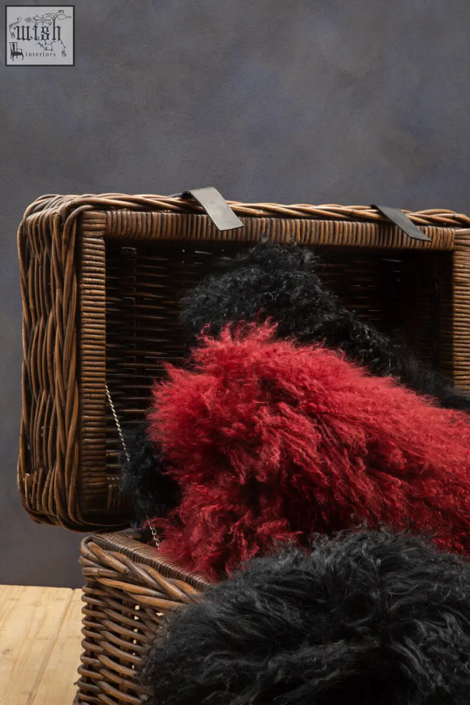 A bosie real mongolian fur black rectangular cushion with vibrant red and black fluffy sheepskin in a wicker basket