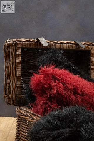 A bosie real mongolian fur black rectangular cushion with vibrant red and black fluffy sheepskin in a wicker basket
