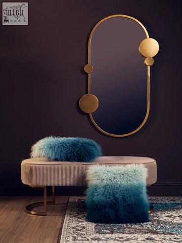 Gold-toned oval mirror with circular accents on dark wall beside bosie real mongolian fur blue ombre square cushion