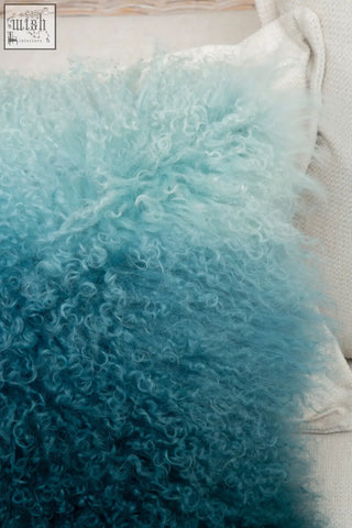 A plush bosie real mongolian fur blue ombre square cushion with curly texture and light to dark teal hues