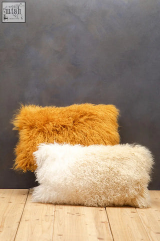 Two rectangular plush cushions in mustard ochre and off-white made with real mongolian lamb fur on wooden floor