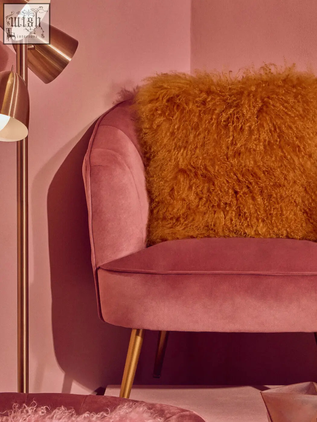 A dusty rose velvet armchair with gold legs featuring a bosie real mongolian lamb fur ochre square cushion