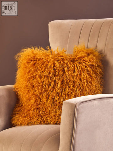 Vibrant orange bosie real mongolian lamb fur square cushion resting on a beige velvet armchair
