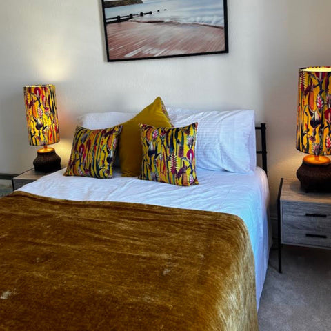 Botanical mustard velvet throw cushion shown with vibrant yellow and black floral lampshades on dark ceramic bases