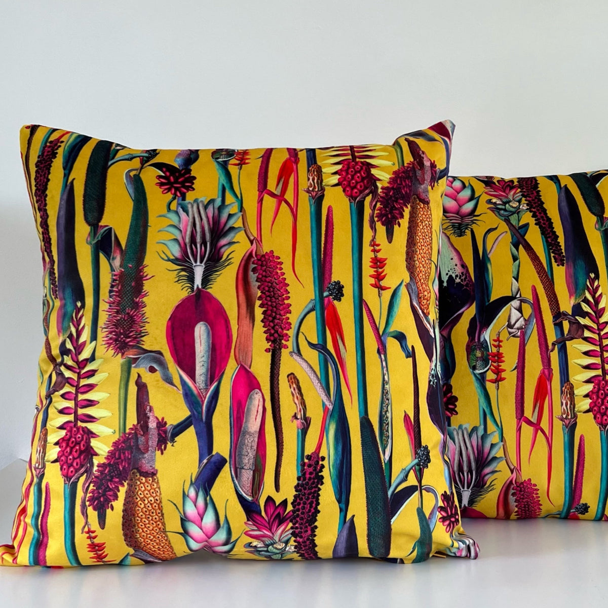 Vibrant botanical mustard velvet throw cushion with bold tropical print in reds pinks and deep greens on plush fabric