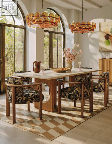 Amber glass chandelier with circular layered discs hangs above boucheron dining table in travertine and solid wood dining area