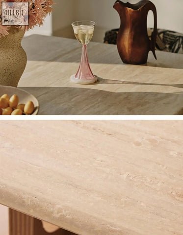 A delicate pink glass wine goblet with white wine on a travertine and solid wood dining table in a dining area