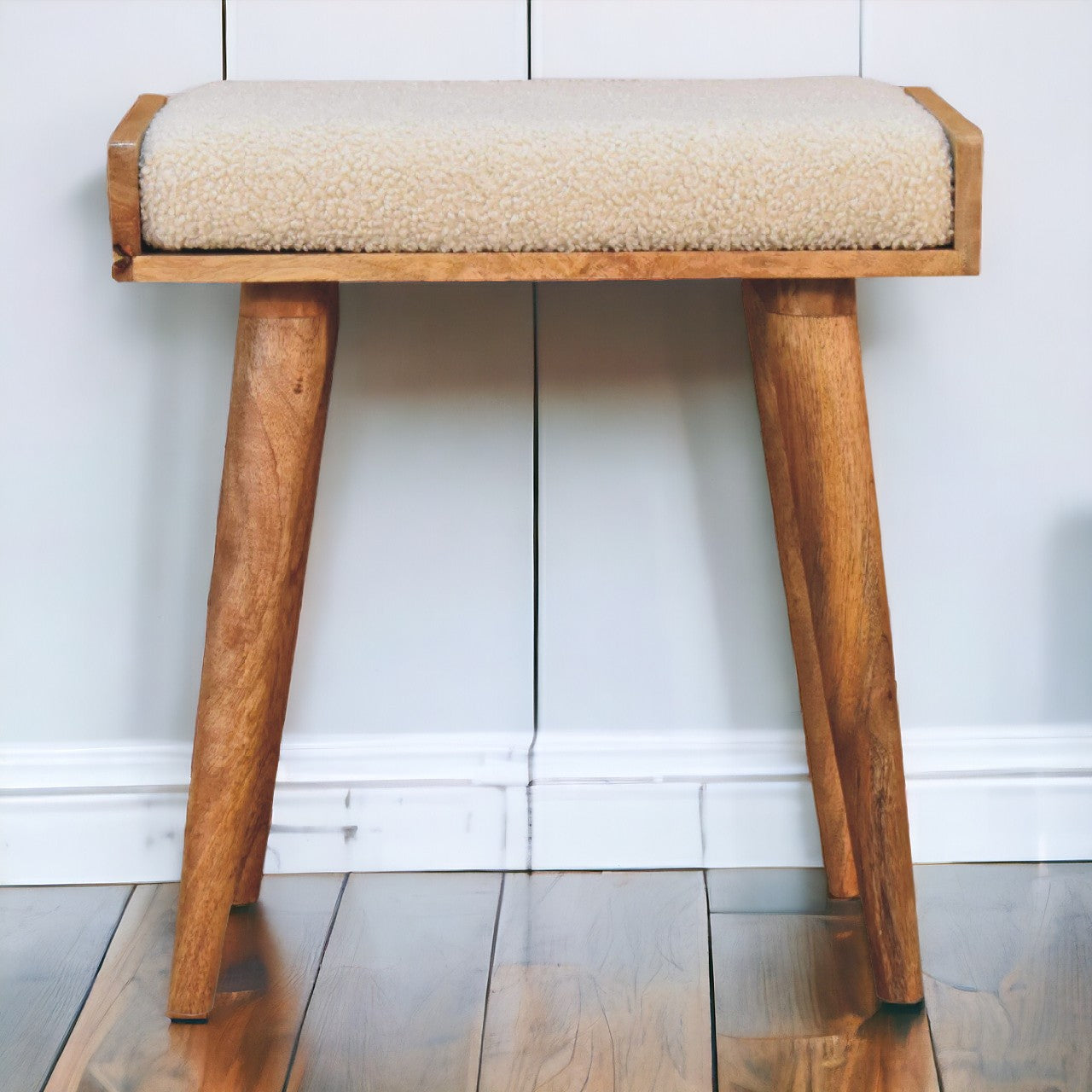 A mid-century modern tray style footstool with boucle cream textured fabric and tapered wooden legs