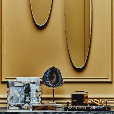 A polished dark blue gold agate sculpture with a glossy finish on a slim metallic stand by bowerbird