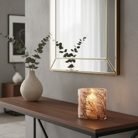 A warm candle glowing inside a medium glass hurricane with an intricate tree branch pattern hurricane candle holder