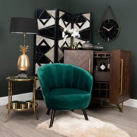Emerald green velvet armchair with plush seat and black legs beside brando acacia wood effect drinks cabinet