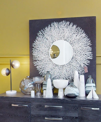 White coral inspired circular mirror with central reflective circle paired with bree grey glass vase on dark background