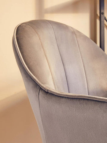 A plush light gray velvet home office chair with vertical stitching on its curved backrest for stylish workspaces
