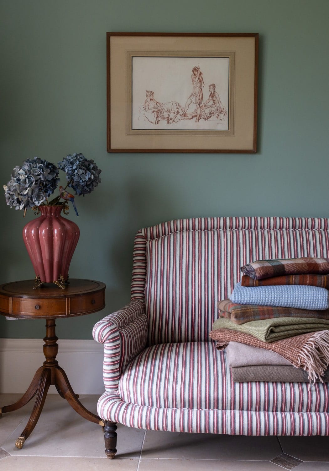 A plush armchair with rolled arms and tufted cream and red stripes paired with a bridgerton regency style vase with two birds