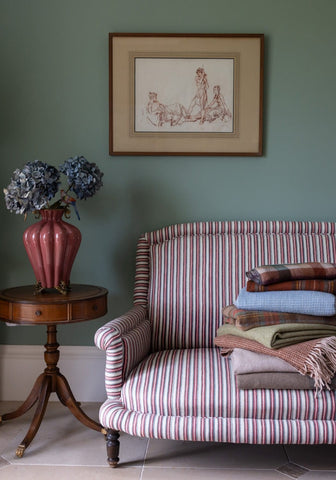 A plush armchair with rolled arms and tufted cream and red stripes paired with a bridgerton regency style vase with two birds