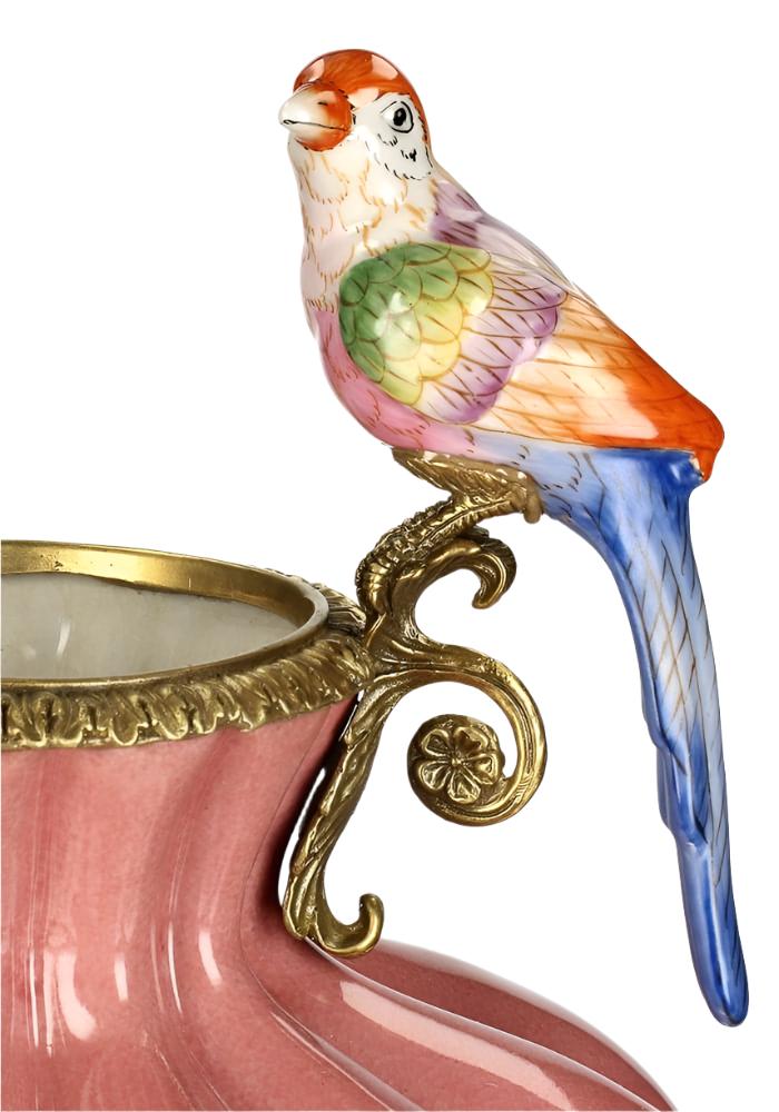 A vibrant hand-painted porcelain parrot on a gold metal handle atop a pink ceramic bridgerton regency style vase