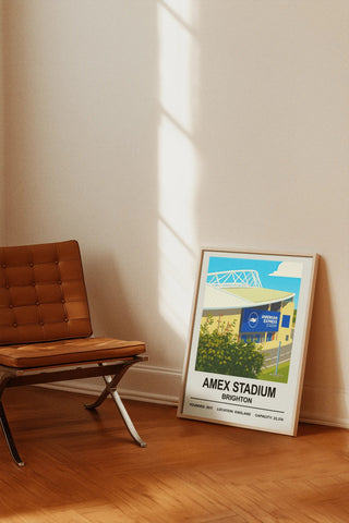 A framed brighton amex stadium print featuring a stylized stadium illustration with greenery and blue sky on cream wall