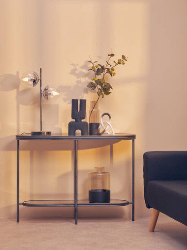 Black minimalist console table with slender metal frame and glass shelves paired with ombre black and white knot sculpture