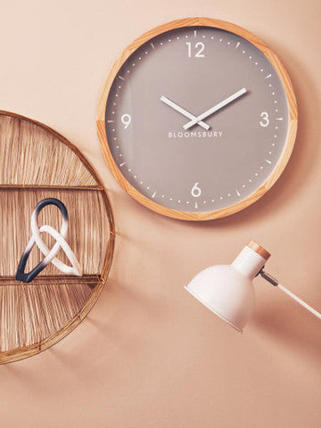 Gray round bloomsbury wall clock with light wood frame and minimalist white hands next to ombre black and white knot sculpture