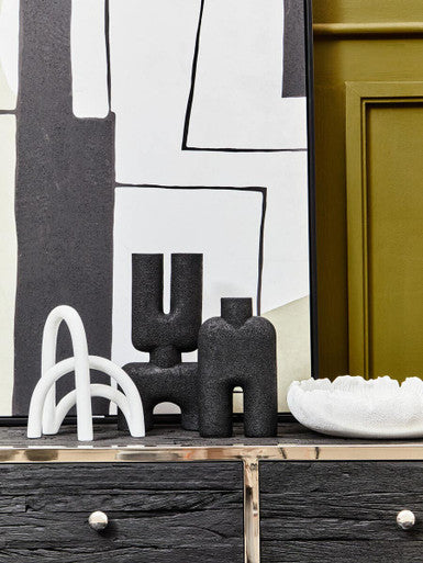 Black textured ceramic vases with abstract humanoid shapes on dark wood table next to broc white textured bowl