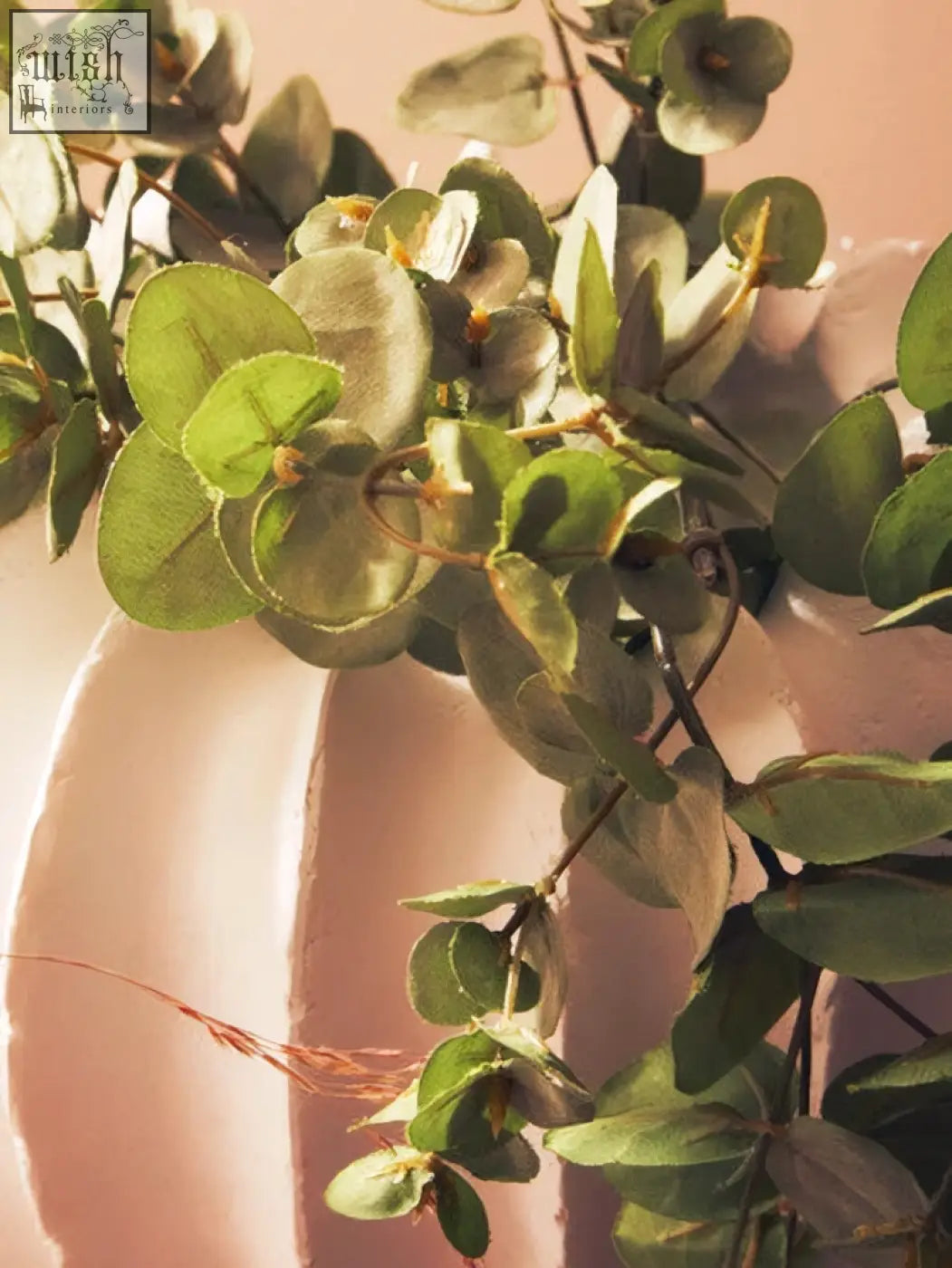 A lush eucalyptus arrangement in a broc white textured vase with silvery green leaves and delicate stems