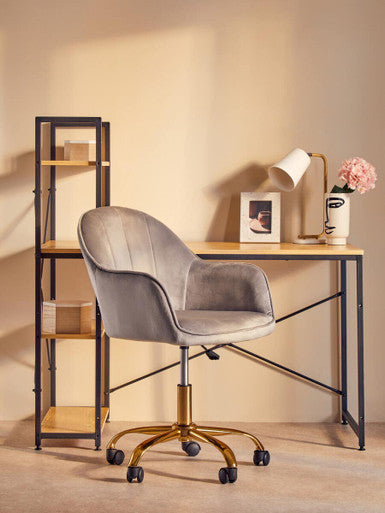 Gray velvet office chair with gold-tone base and casters next to a bruin table lamp with white metal base