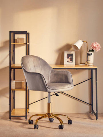 Gray velvet office chair with gold-tone base and casters next to a bruin table lamp with white metal base
