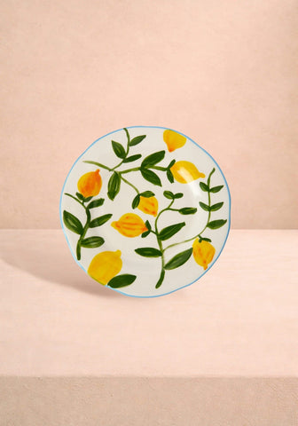A white ceramic lunch plate with hand-painted yellow lemons green leaves and a thin blue rim inspired by matisse