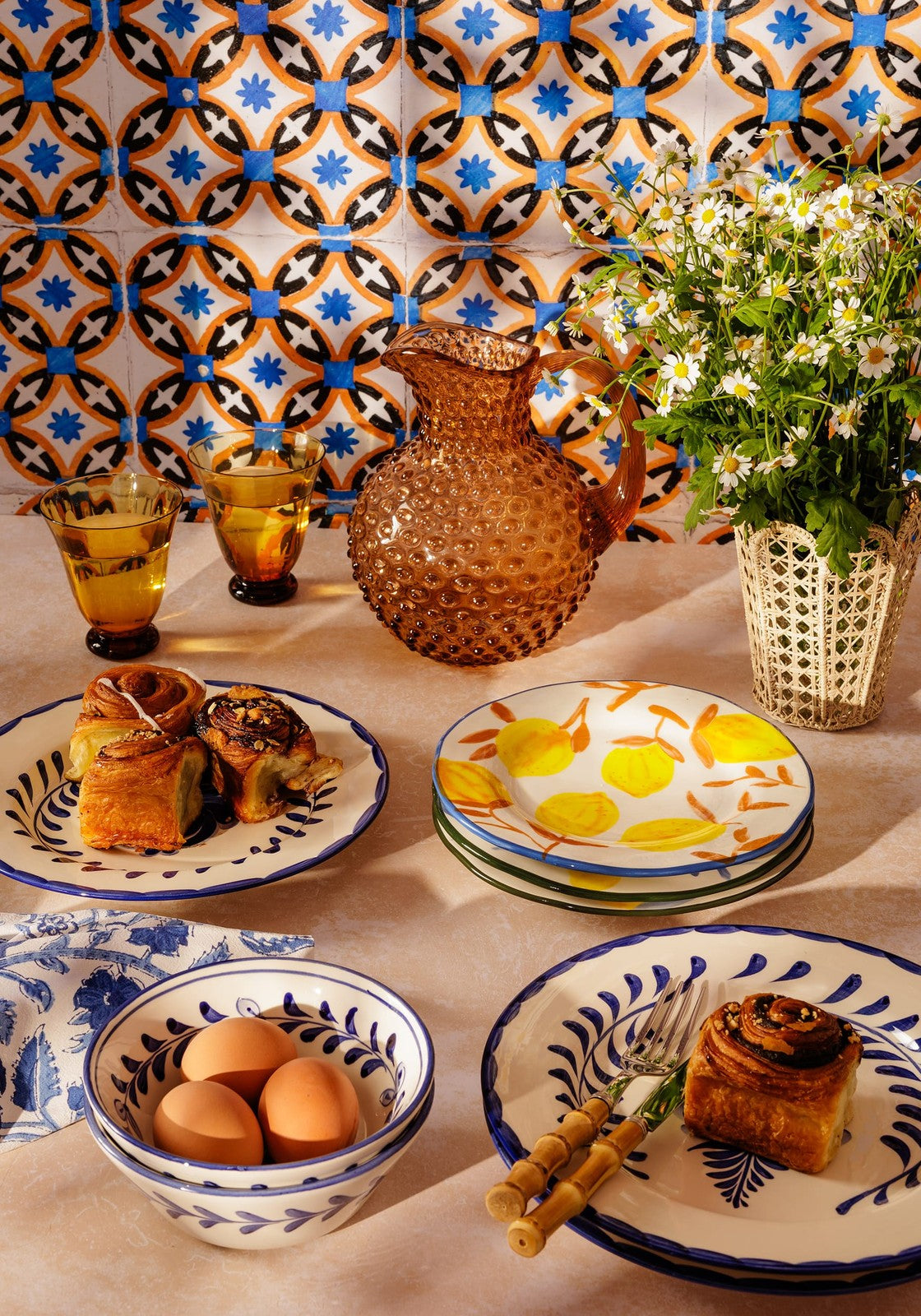Amber-hued textured glass pitcher with bulbous body and curved handle next to buds in may hand-painted lunch plates set
