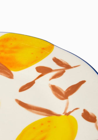 A white ceramic lunch plate with a blue rim featuring hand-painted yellow lemons and brown leaves inspired by matisse