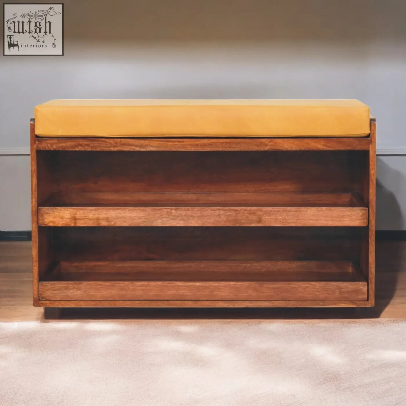 A mustard yellow velvet cushioned shoe storage bench with solid mango wood frame and two open shelves for storage