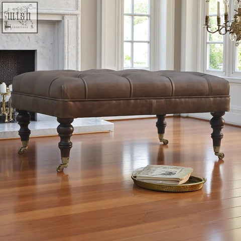 Brown buffalo leather storage bench with rectangular form tufted top dark wooden legs and brass casters for additional seating