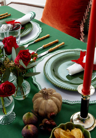 Burgundy velvet cushion cover with tassels paired with green ceramic plates on a matching green tablecloth