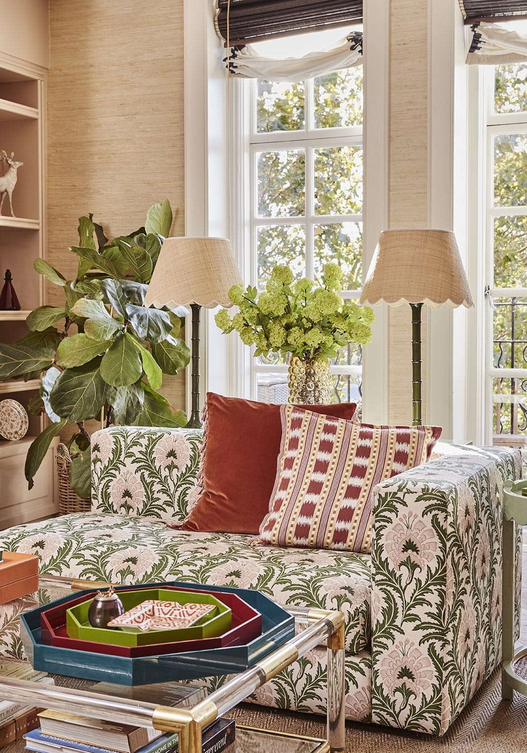 A burgundy velvet cushion cover with tassels on a plush green and cream floral sofa with red velvet cushions