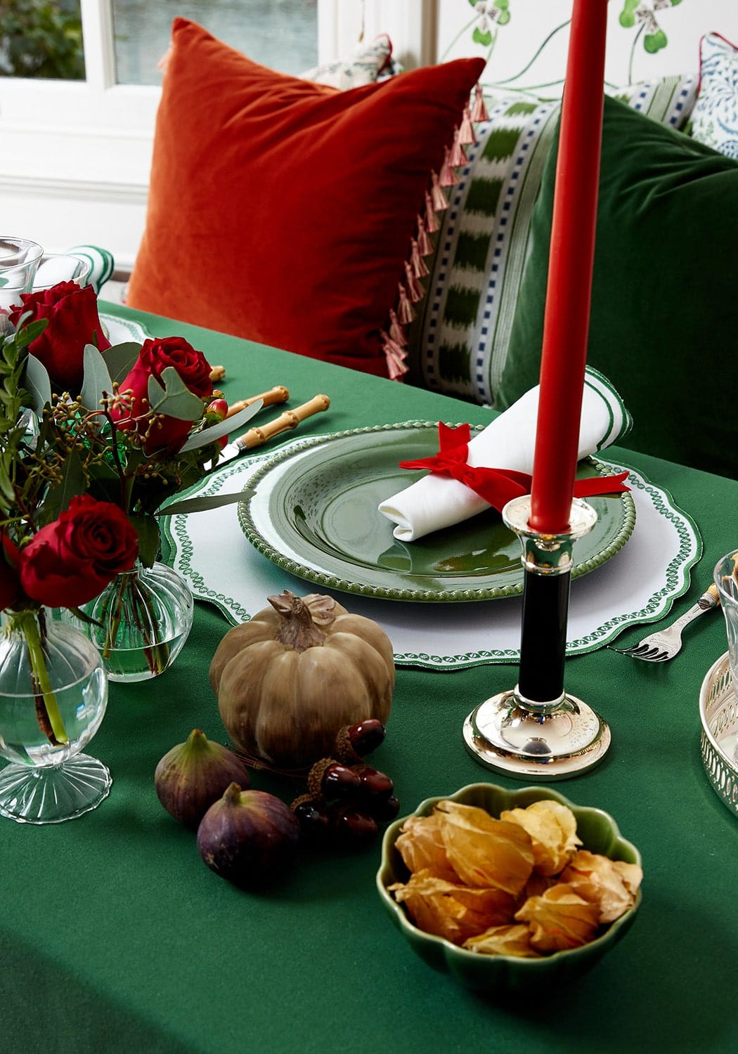 A tall red candle in a silver holder next to a burgundy velvet cushion cover with tassels for cozy decor