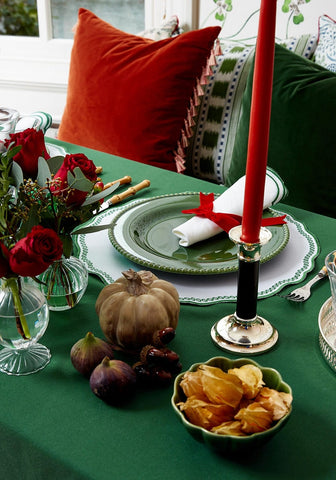 A tall red candle in a silver holder next to a burgundy velvet cushion cover with tassels for cozy decor