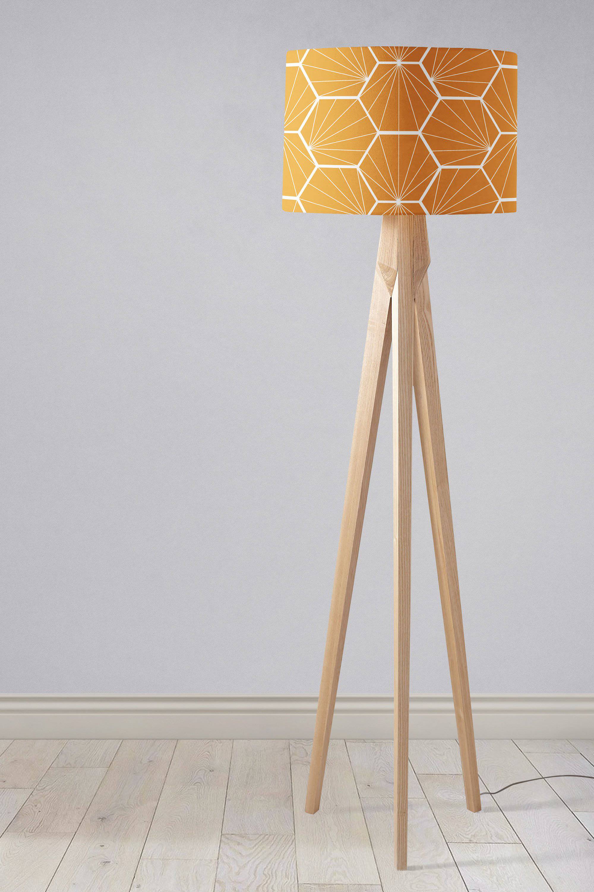 A modern tripod floor lamp with a butterscotch yellow geometric hexagons lamp shade and light wood legs perfect as a table lamp