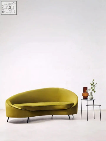 A sleek olive green velvet sofa with curved design and black metal legs next to a calcita small speckled green vase