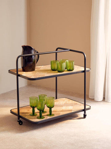 Black metal serving cart with two wooden shelves holding green glassware and a black glazed pitcher on each level