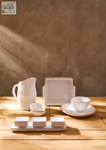 White glazed cereal bowl set with pitcher square plates and matching bowls on wooden surface in terracotta style