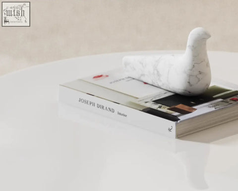 A white marble dove figurine with gray veining resting on a book on the calloway nesting coffee table set