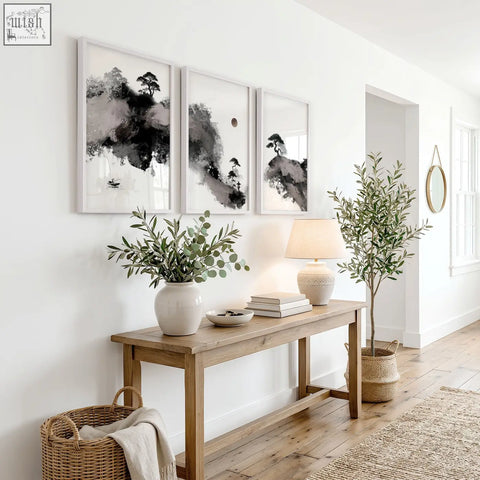 A white ceramic vase with green eucalyptus branches complements calming wall art featuring maroon sun and black pine trees
